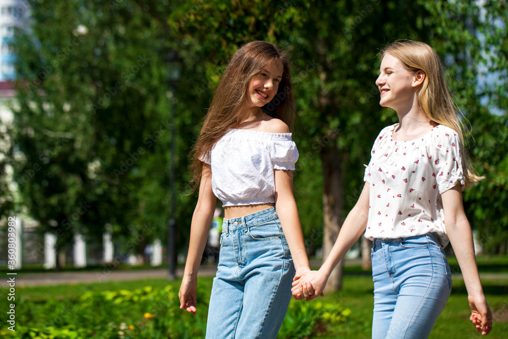 Two happy girlfriends teenagers are walking in the summer park. Two happy girlfriends teenagers are walking in the summer park.