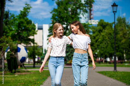 Two happy girlfriends teenagers are walking in the summer park.