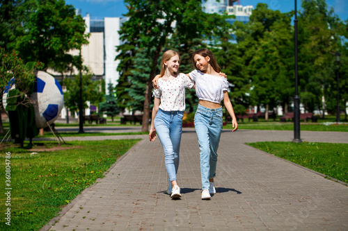 Two happy girlfriends teenagers are walking in the summer park. © Andrey_Arkusha