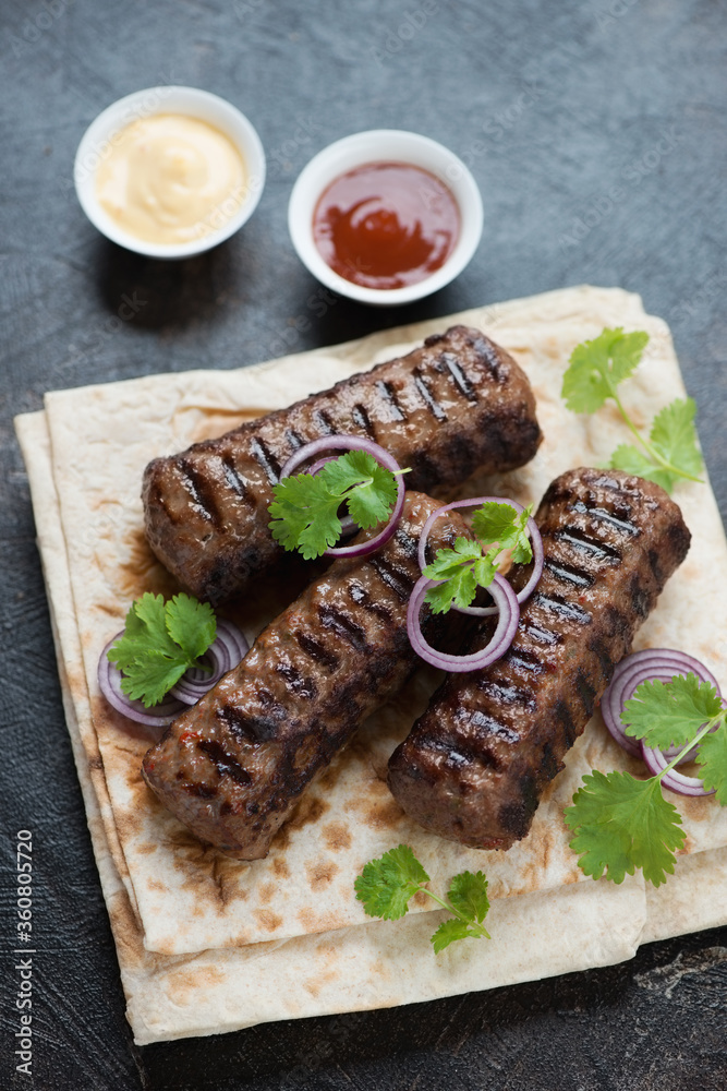 Roasted marbled beef kabobs with lavash flatbread over dark brown stone background, vertical shot, selective focus