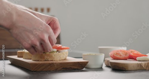 young man making bruschetta with tomato, pesto and mozzarella on olive board