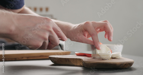 man slicing mozzarella ball on olive wood board