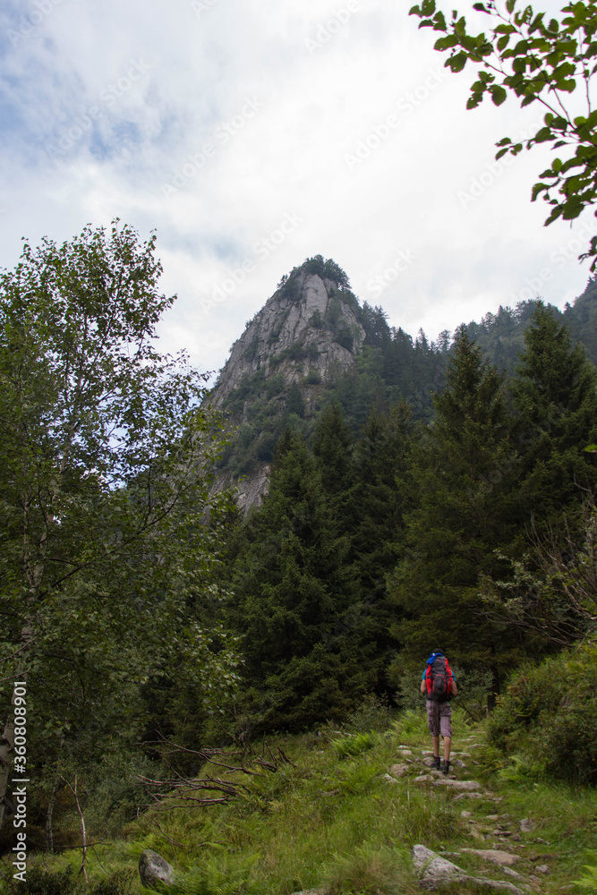 The view of a man walking on a hiking path with mountain peak on background.