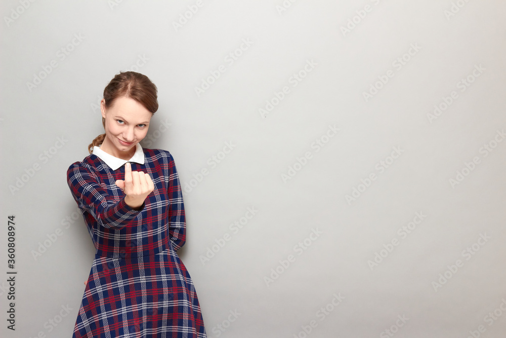 Portrait of cheerful girl beckoning someone with finger and smiling