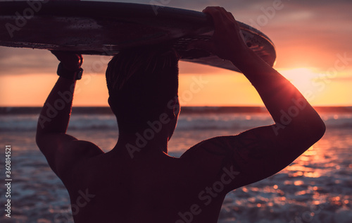 Close up of surfer holding his surfboard over his head looking at the sea during an amazing sunset