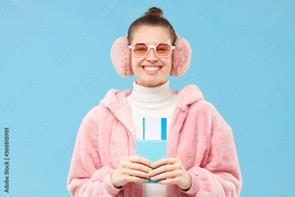 Young happy female holding passport with tickets, ready to go travelling in winter, isolated on blue background. Christmas tour or journey and tourism concept Young happy female holding passport with tickets, ready to go travelling in winter, isolated on blue background. Christmas tour or journey and tourism concept