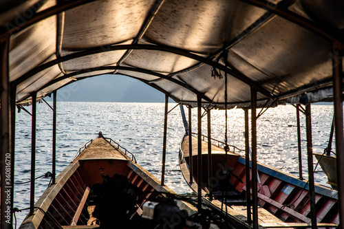 Two empty long-tailed boats floating on the lake with rays of light in the morning. A look from the inside of vehicle to the lake and mountain. 