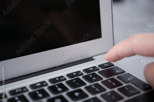 Pushing the power switch on a keyboard of a grey notebook with a finger by male hand
