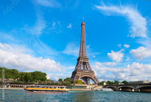 Cityscape of Paris, France. Eiffel tower on a sunny day, with tourist boats on river Seine. Bright sunny day with feather clouds in blue sky.