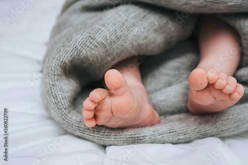 A small child sleeps on a white bed, covered with a gray plaid close-up. The legs of the newborn. Photography, concept.