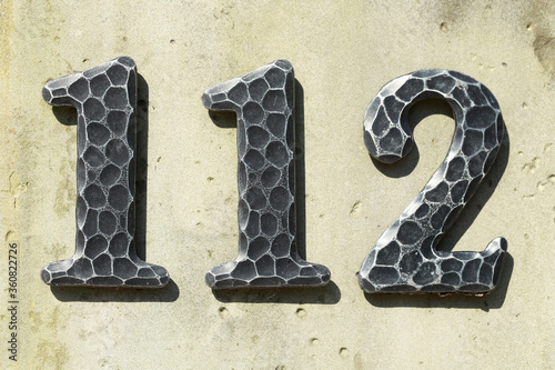 Schwarzes eisernes  Hausnummernschild Nummer Hundertzwölf auf einer hellen Hauswand photo