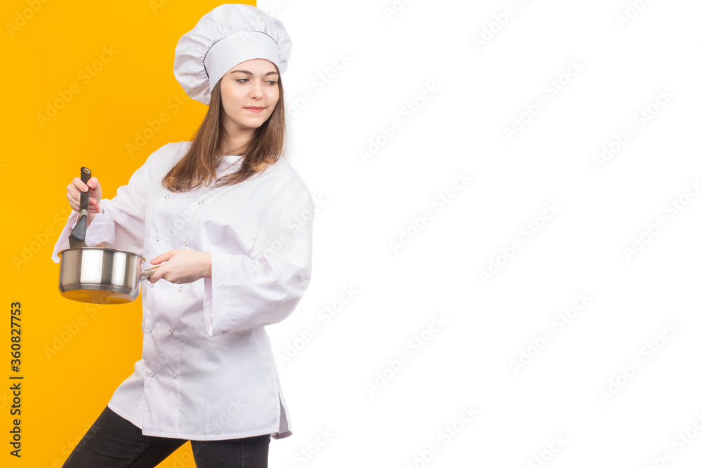 Chef woman is looking at a white banner. Girl in a suit and a cook hat. Chef holds a pan and a culinary spatula. Concept - cookbook. Chef teaches to cook. A young woman is learning how to cook. Chef woman is looking at a white banner. Girl in a suit and a cook hat. Chef holds a pan and a culinary spatula. Concept - cookbook. Chef teaches to cook. A young woman is learning how to cook.
