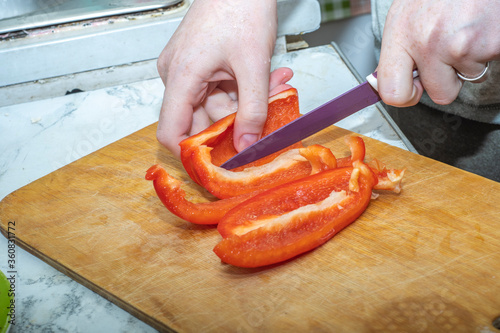 Close-up - hands cut red pepper with a knife on a wooden board