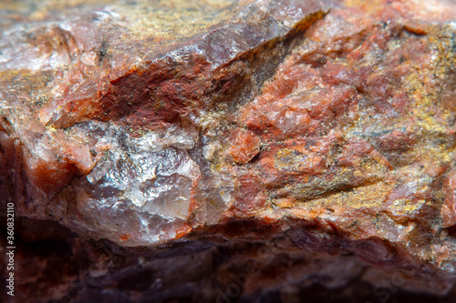 Photograph of a granite surface interspersed with transparent mica in soft focus at high magnification. Fine texture of natural mineral of pink color with blurred background.