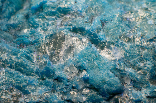 Photo of a stone surface interspersed with transparent mica in soft focus at high magnification. Fine blue mineral texture with blurred background.