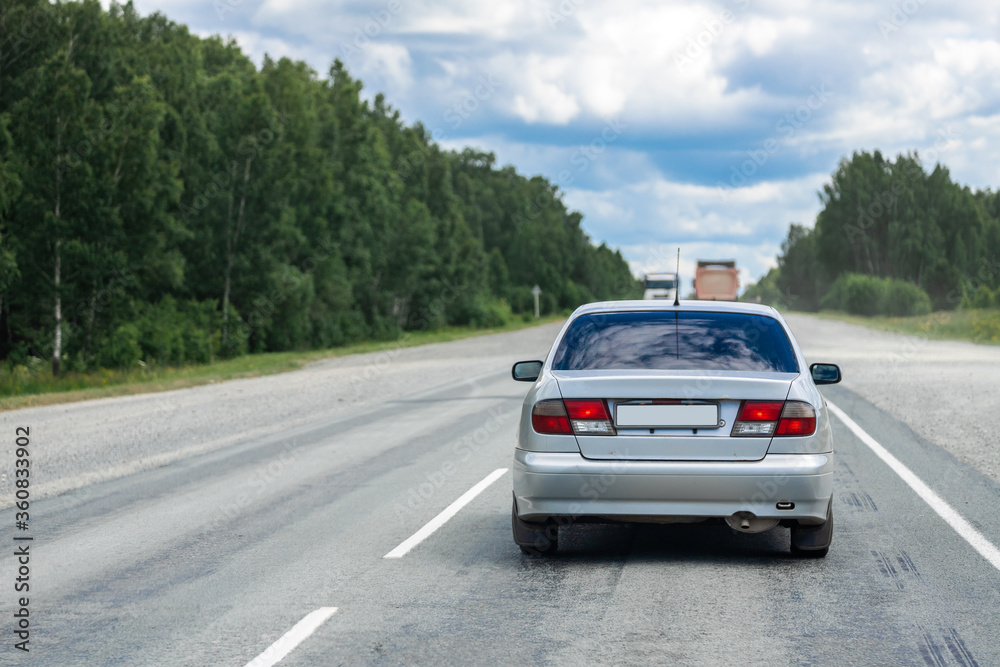 Car sedan rides on an asphalt road in the background forest landscape and car traffic from trucks. The concept of moving from city to city in your car. Traveling by car