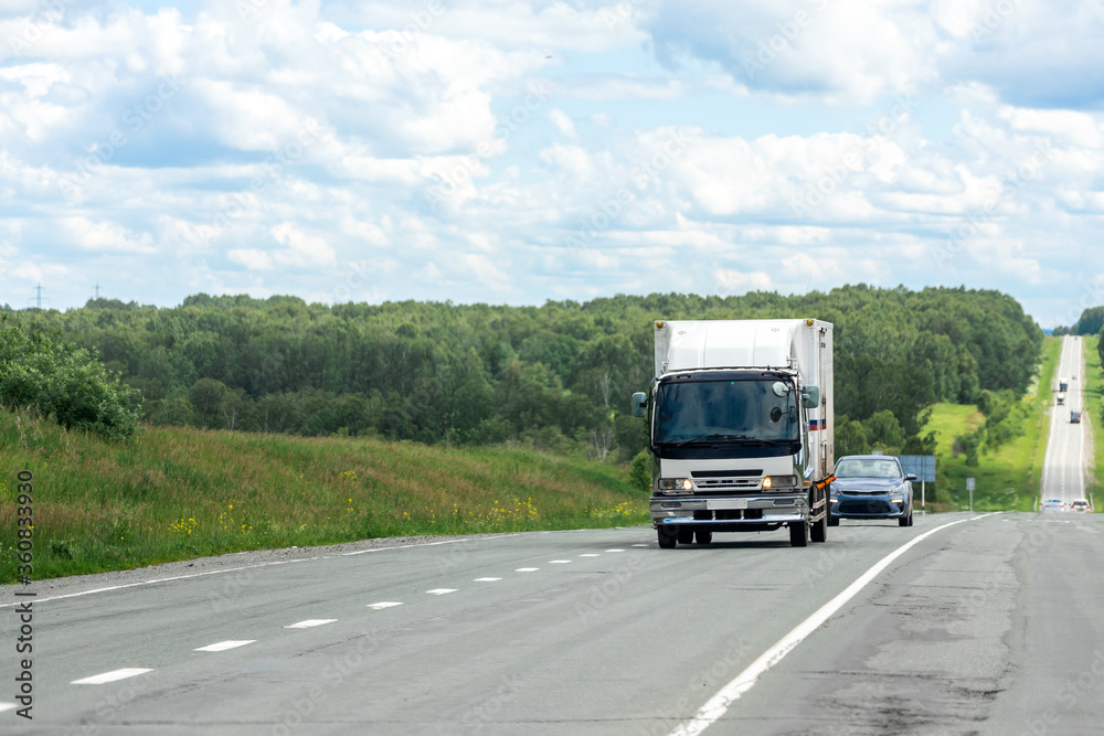 Big truck moving on the highway, against the background of the village and forest landscape. Concept of export-import,transportation, national delivery of goods Big truck moving on the highway, against the background of the village and forest landscape. Concept of export-import,transportation, national delivery of goods