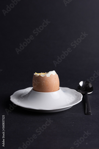 Braunes Frühstücksei im Eierbecher mit Loffel rechts am Rand auf schwarzen Hintergrund photo