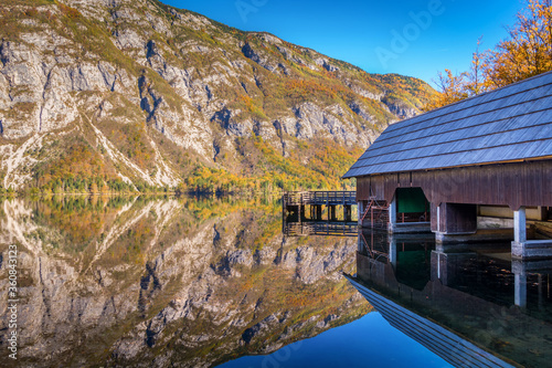 Reflection in water of beautiful Bohinj lake in Slovenia. Boathouse on the right side of frame. Alps mountains reflected in water. Idyllic and pristine nature, famous tourist spot