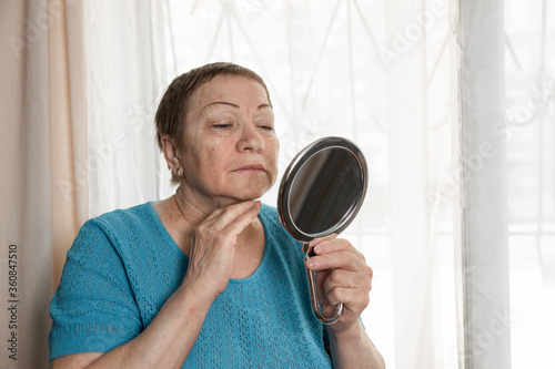 An old woman looks at her face in the mirror,