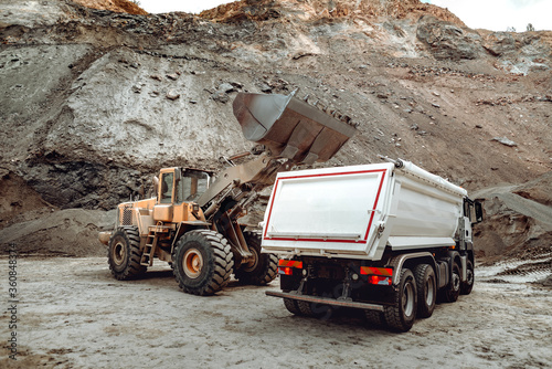 Industrial dumper trucks and wheel loader bulldozer working on highway construction site  loading and unloading gravel and earth. heavy duty machinery activity.