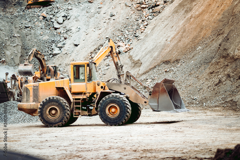 Industrial heavy duty wheel loader on quarry site transporting and loading gravel into dumper trucks