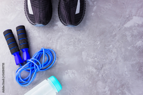 Fitness concept with sneakers  jump rope and bottle of water. Sports equipment on a gray background. Healthy lifestyle concept. Copy space. Top view