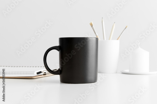 Black mug mockup with workspace accessories on a white table.