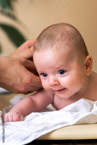 Obraz na płótnie Little blue eyed caucasian baby is getting his care and hygiene routine at home while lying down on his belly. Smiling and enjoying his tummy time. w salonie