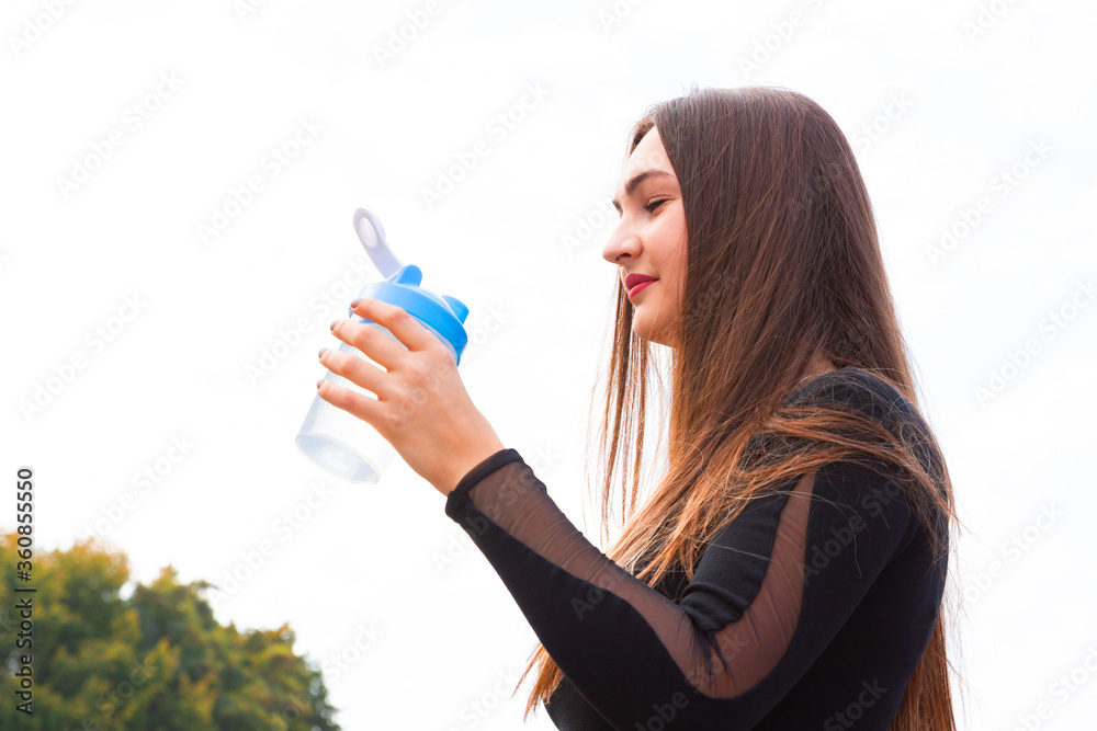 Beautiful young girl drinks water in the park after exercise. Portrait of sporty woman drinking water in park after jogging. Female athlete after training workout. Copy space Beautiful young girl drinks water in the park after exercise. Portrait of sporty woman drinking water in park after jogging. Female athlete after training workout. Copy space