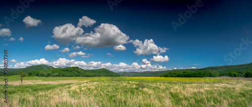 Summer landscape with green meadows and hills, and a blue sky with clouds