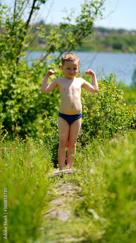 Portrait of a funny little boy standing barefoot on path near pond
