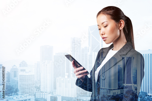 Prosperous astonishing young Asian business woman in suit texting phone the details of corporate meeting. Kuala Lumpur cityscape. The concept of business communication. Double exposure. photo