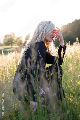 Donna bella e bionda che sorride in un campo, con l'erba alta, in controluce