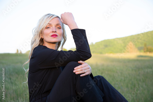 Giovane donna sorridente bella e bionda vestita di nero seduta in un parco