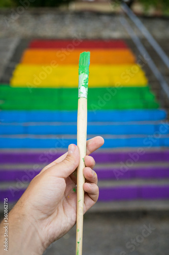 Hand holding a green brush in front of a stairs with the homosexual flag