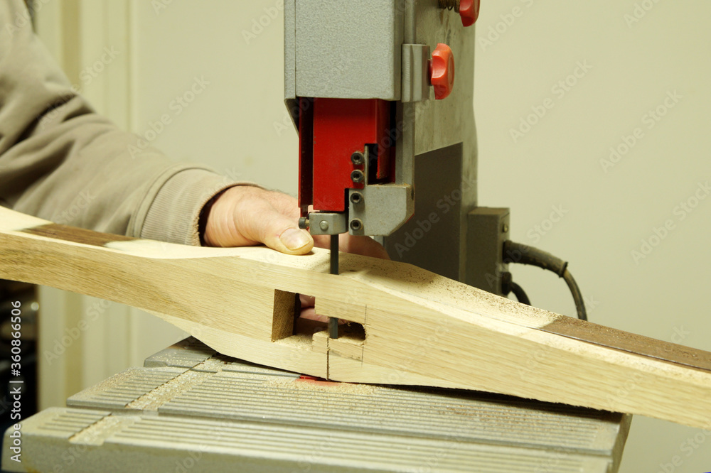 Crossbow Making. close up of making cross bow in workshop with jigsaw, male crossbow-maker at band saw. arbalist, arbalest. hands of a Carpenter, worker sawing. A craftsman cutting wood with bandsaw. Crossbow Making. close up of making cross bow in workshop with jigsaw, male crossbow-maker at band saw. arbalist, arbalest. hands of a Carpenter, worker sawing. A craftsman cutting wood with bandsaw.