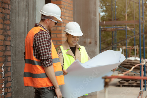 The construction Manager and engineer, wearing work vests and hard hats, study construction documentation on the construction site