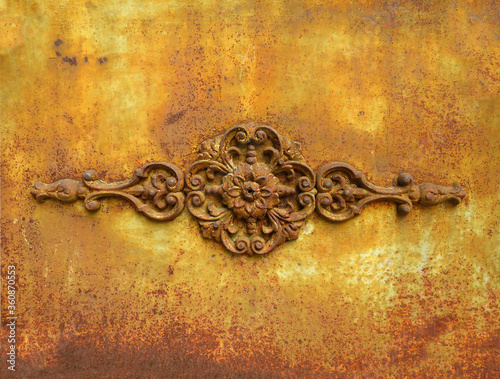 Antique metal ornamental detail on rusty yellow wrought iron wall. Rusty painted old ornate decorative wrought metal grill in dilapidated state. Background and textures.