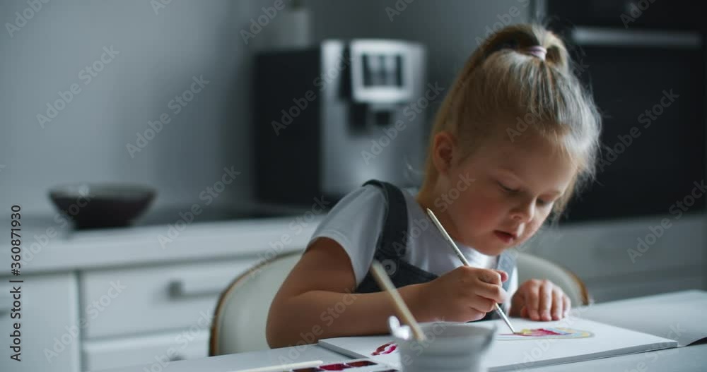 A girl child of 4 to 7 years old sits in the house and paints on paper. The child draws a rainbow with paints. A keen child is busy with his own business. A girl child of 4 to 7 years old sits in the house and paints on paper. The child draws a rainbow with paints. A keen child is busy with his own business.