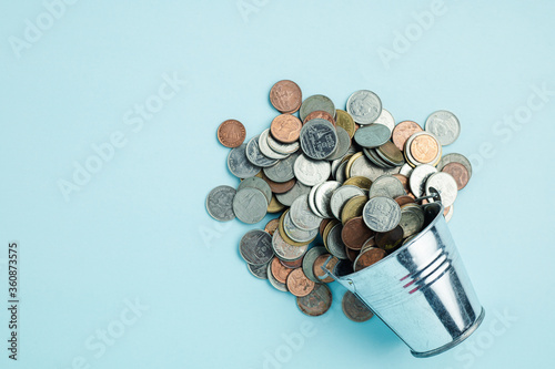 Full of money coins in a tin bucket on blue background for investment, business, finance and saving money concept