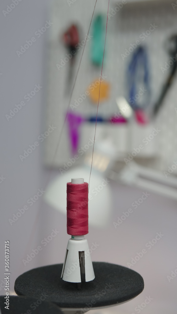 A reel of red thread on a professional sewing machine. The sewing shop. Tailor shop equipment. Sewing instruments and equipment. Selective focus. A reel of red thread on a professional sewing machine. The sewing shop. Tailor shop equipment. Sewing instruments and equipment. Selective focus.