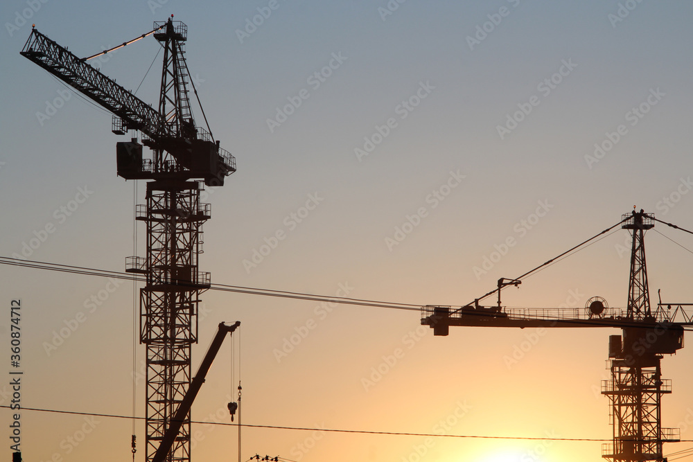 Cranes at a construction site against the backdrop of the setting sun