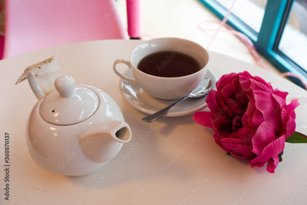 ceramic white teapot and Cup of tea on the table in the cafe and decor in the form of a pink rose flower ceramic white teapot and Cup of tea on the table in the cafe and decor in the form of a pink rose flower