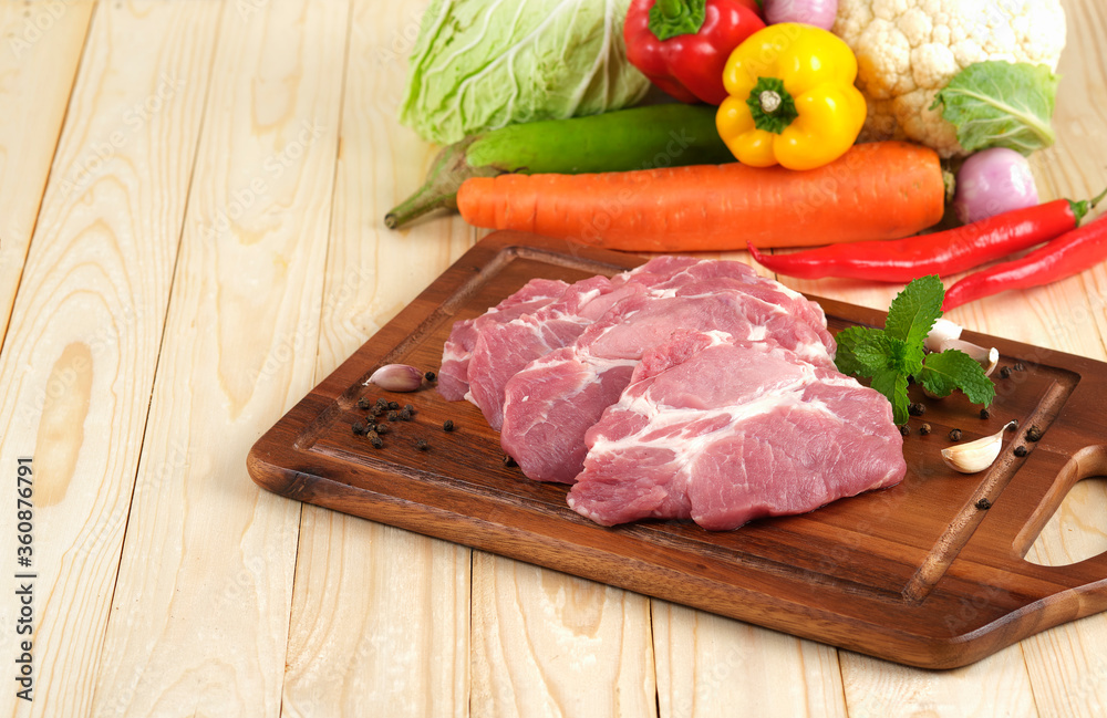 Pork neck Slice on wooden plate on wooden table with vegetables on background Pork neck Slice on wooden plate on wooden table with vegetables on background