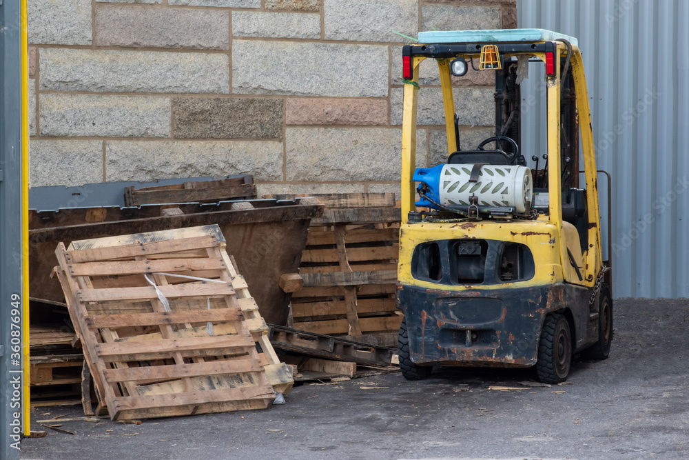 Obraz premium Yellow metal forklift and old used wooden palettes in an outdoor warehouse.