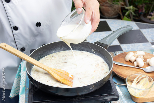 Fotografia, Obraz Chef pouring whipping cream in the pan for cooking mushroom cream soup