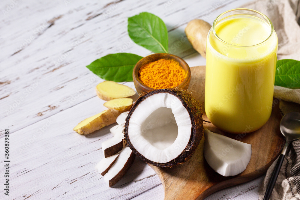 Cup of Healthy ayurvedic drink golden coconut milk turmeric iced latte with curcuma powder on kitchen table. Copy space. Cup of Healthy ayurvedic drink golden coconut milk turmeric iced latte with curcuma powder on kitchen table. Copy space.