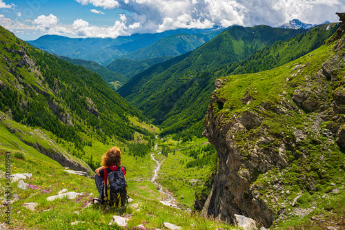 Woman with backpack resting on mountain top, looking at view dramatic landscape valley summer activity fitness wellbeing freedom concept, rear view © fabio lamanna