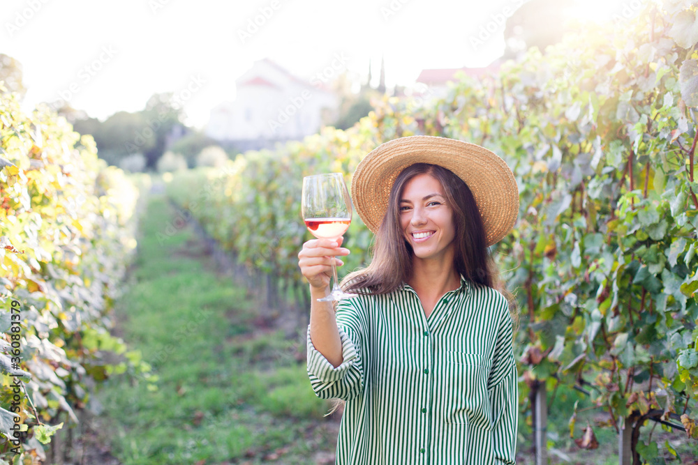 Woman with wineglass of pink wine in vineyard at sunset. Wine tasting in winery. Traveler enjoying local tourism and summer vacation. Happy celebration and social distance. Authentic lifestyle.